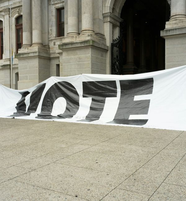A sagging "VOTE" banner on the ground outside a buildi
