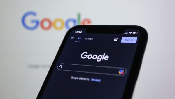 A smartphone showing the Google app on a black screen, against a white screen showing Google desktop sear