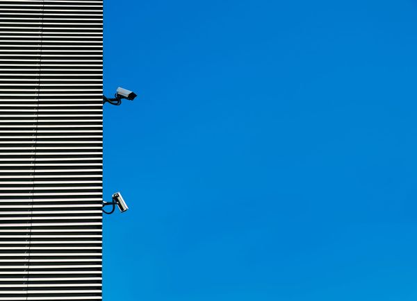 Surveillance cameras on the side of a building next to a blue sky