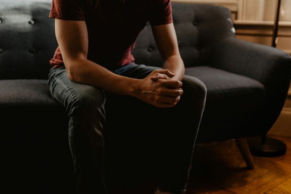 A cropped photo of a man shown from the neck down sitting on a therapists' couch with his hands folded
