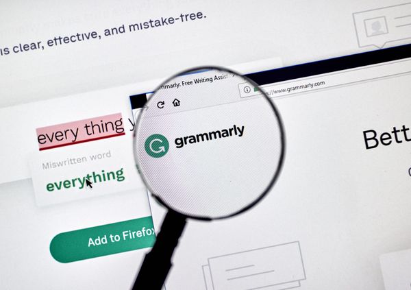 A magnifying class over the Grammarly wordmark and logo displayed on a monitor. On the screen Grammarly is highlighting a mistake in the text