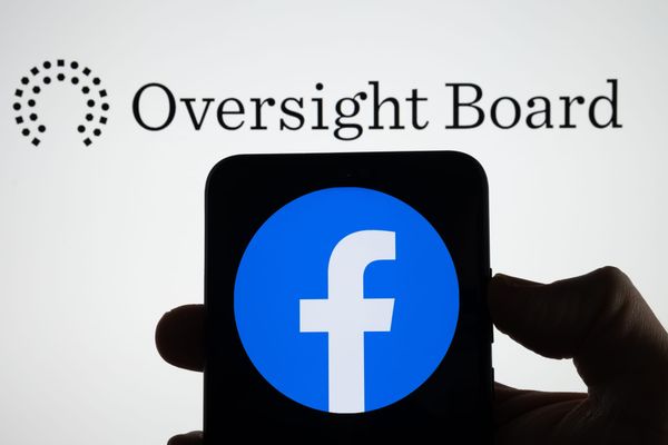 The Oversight Board logo behind the Facebook logo depicted on a smartphone in shadow