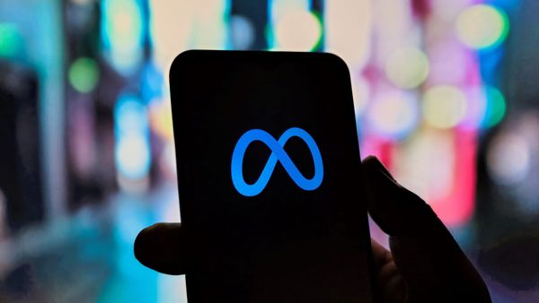 The Meta logo shown on a black smartphone in a hand in silhouette against a colorful bokeh background