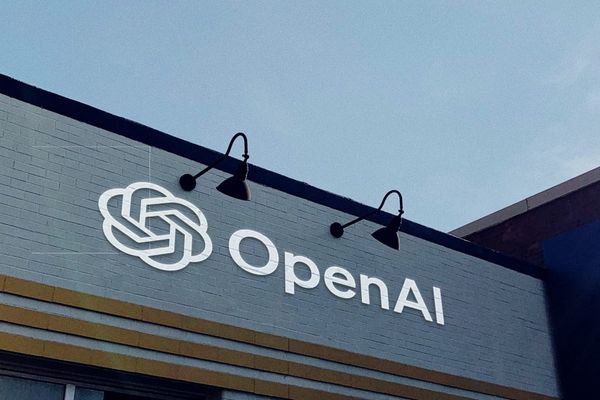 A gray brick wall with the OpenAI logo and wordmark painted on it