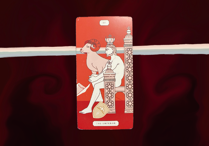 A tarot card showing The Emperor (IV) - a crowned figure with ram horns sitting on an ornate throne with decorative pillars, set against a dark red and blackish background.