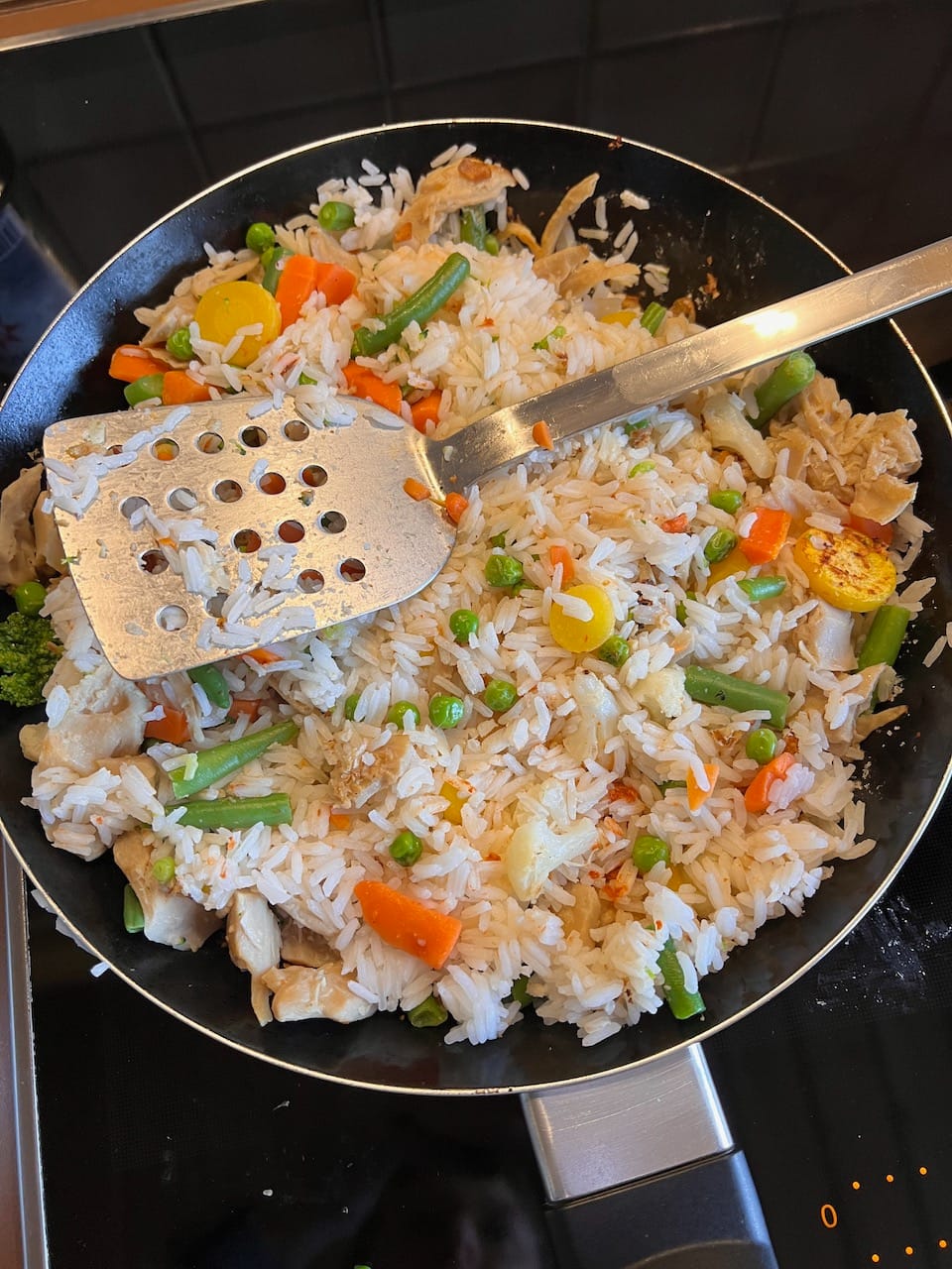 Eine Pfanne mit Pfannenwender auf Herd. In der Pfanne: Reis, Gemüse und Fleisch (vegan)