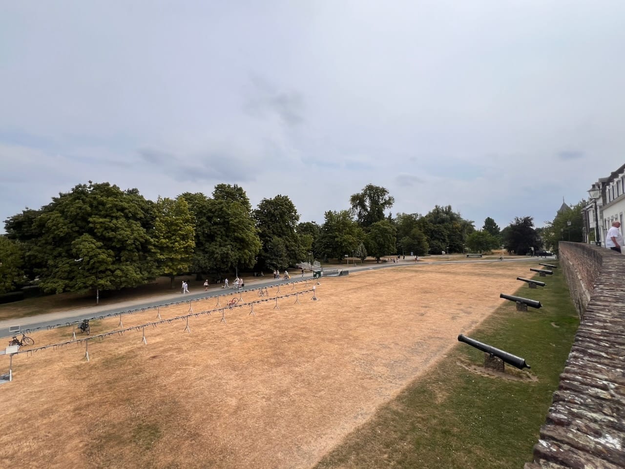 Eine trockene Wiese an einer Mauer, vor der alte Kanonen stehen