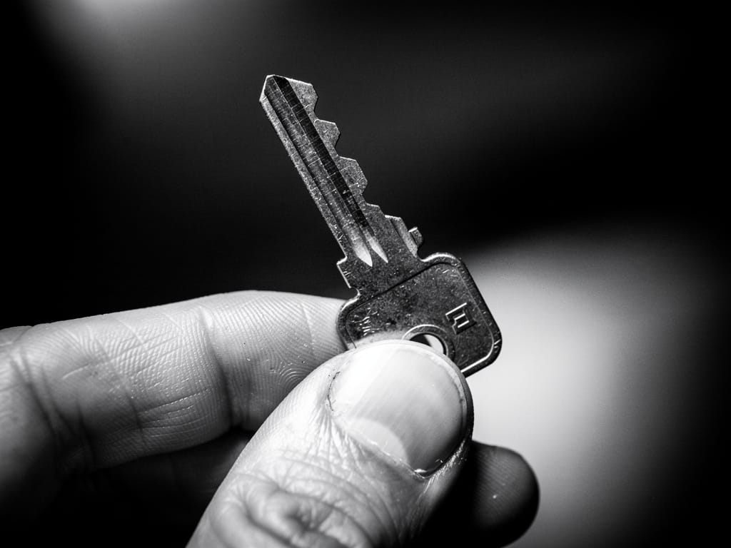 A single old key held between two fingers in a black and white photo