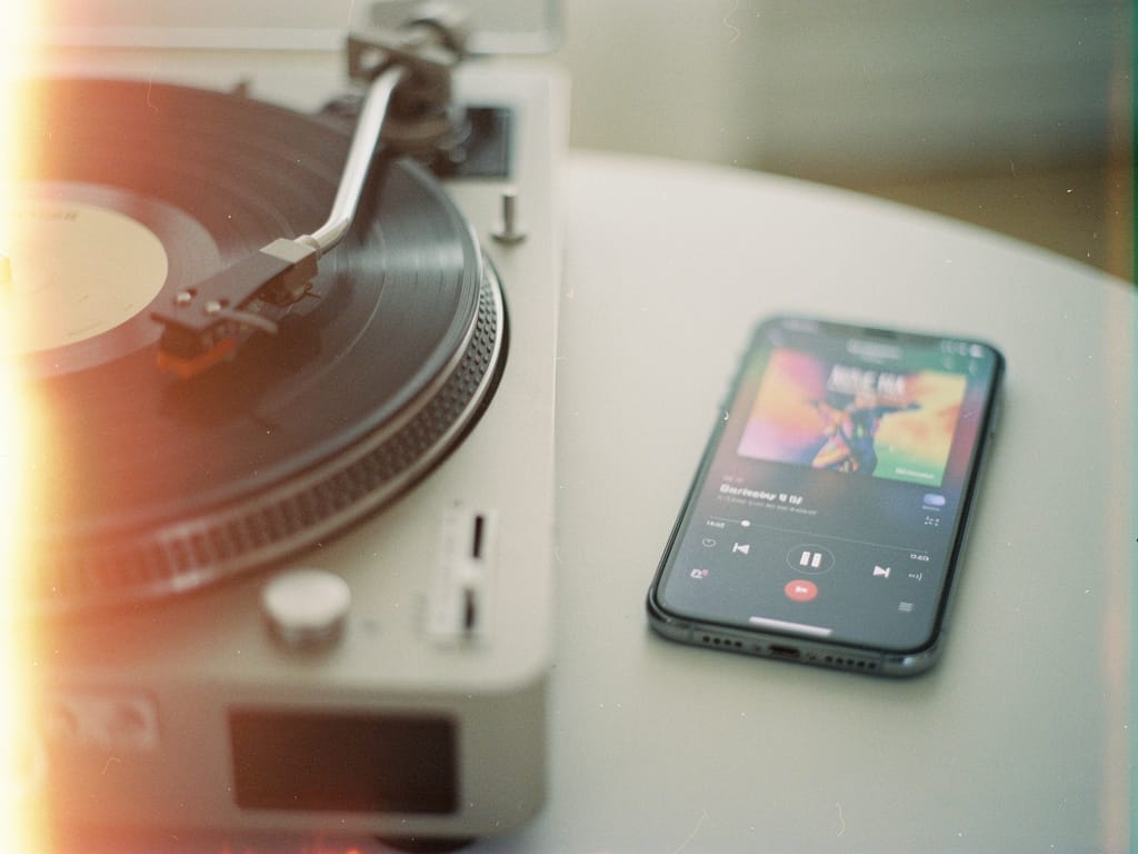 A vinyl record player next to a smartphone with a music app