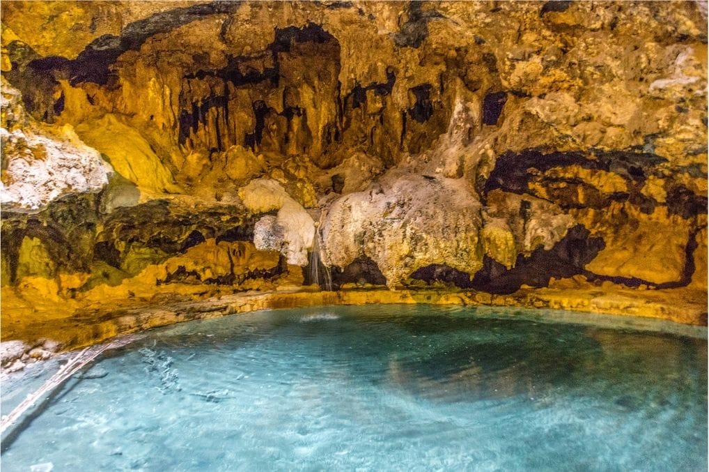Clear turquoise water beneath golden-lit cave walls, with a small trickle of water falling into the pool at Cave and Basin.