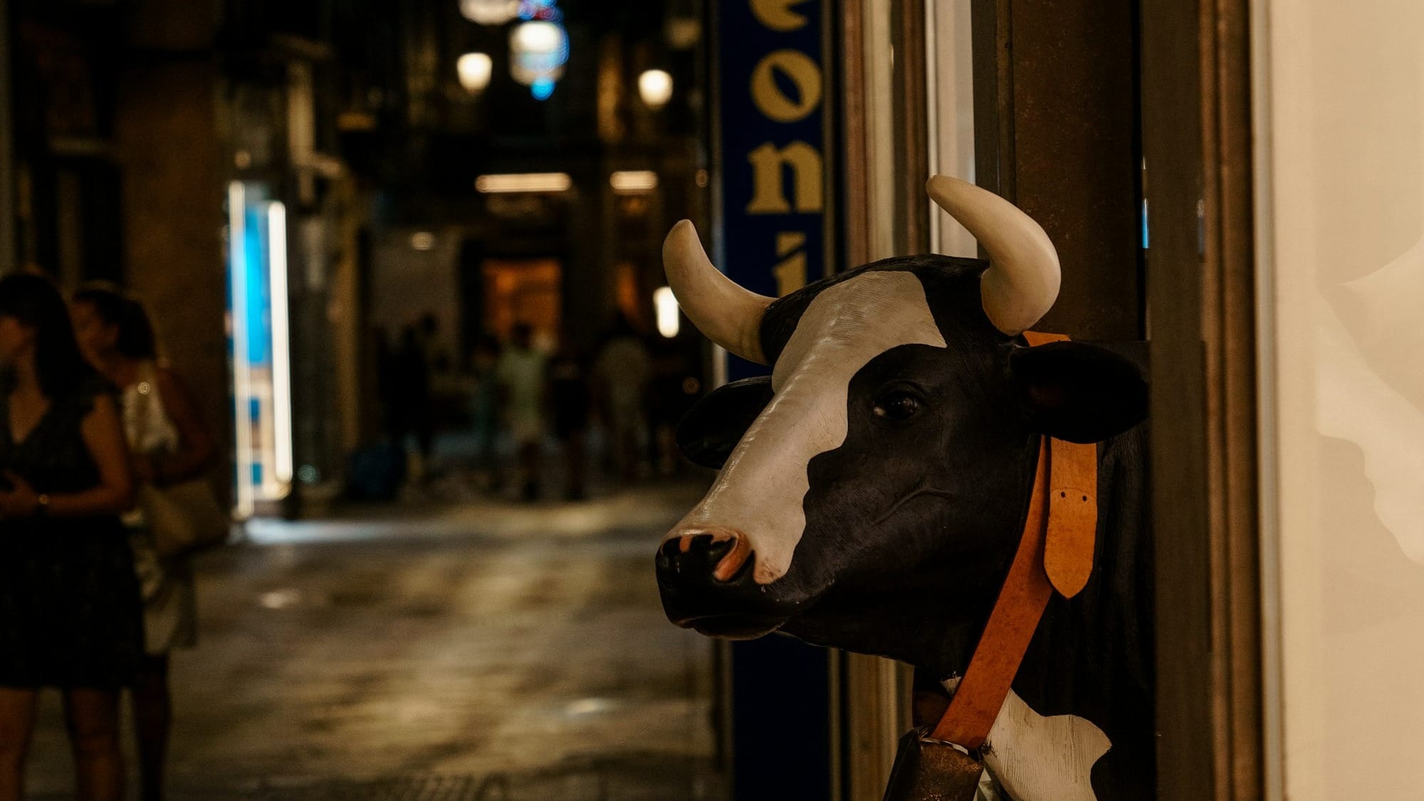a life-sized model of a cow with its head sticking out of a doorway on a city street at night 