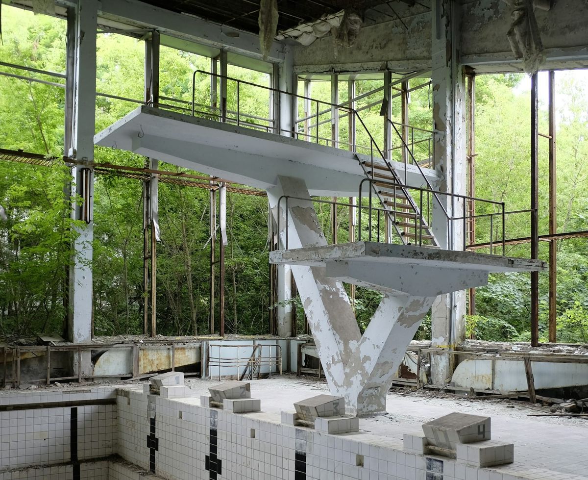 two derelict diving boards at the ruins of a swimming center surrounded by dense forest