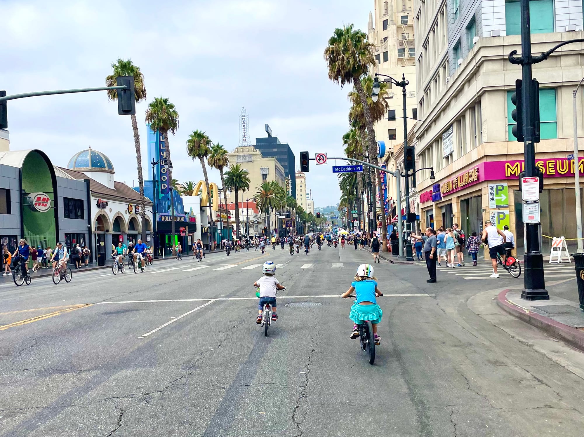 Two young kids on bikes riding down Hollywood Boulevard lined with palm trees during CicLAvia open streets event