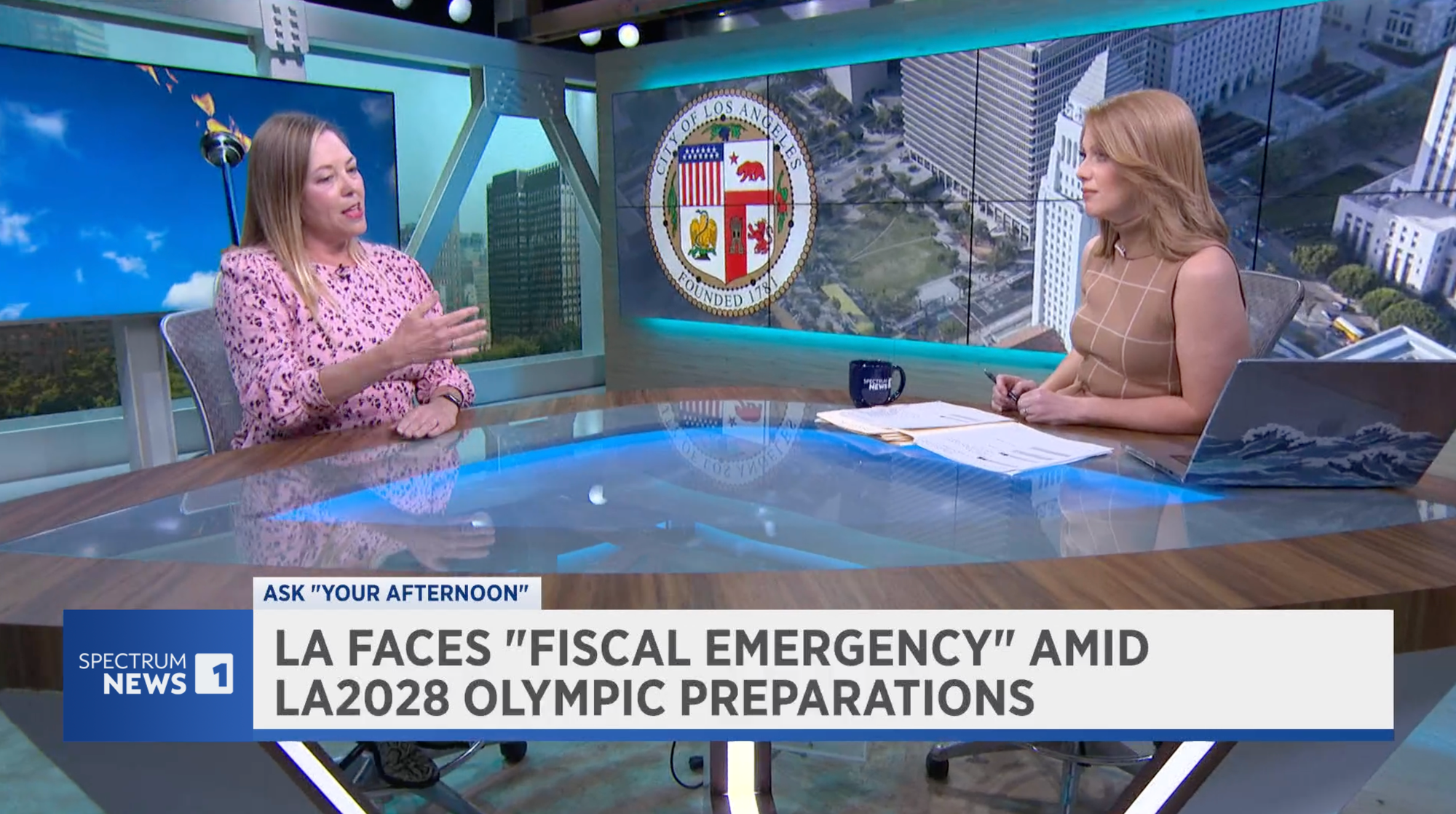 It's me wearing a pink dress sitting at a news desk with Kate Cagle on her local news show talking about Olympics preparations. The chyron says LA FACES FISCAL EMERGENCY AMID LA2028 OLYMPIC PREPARATIONS