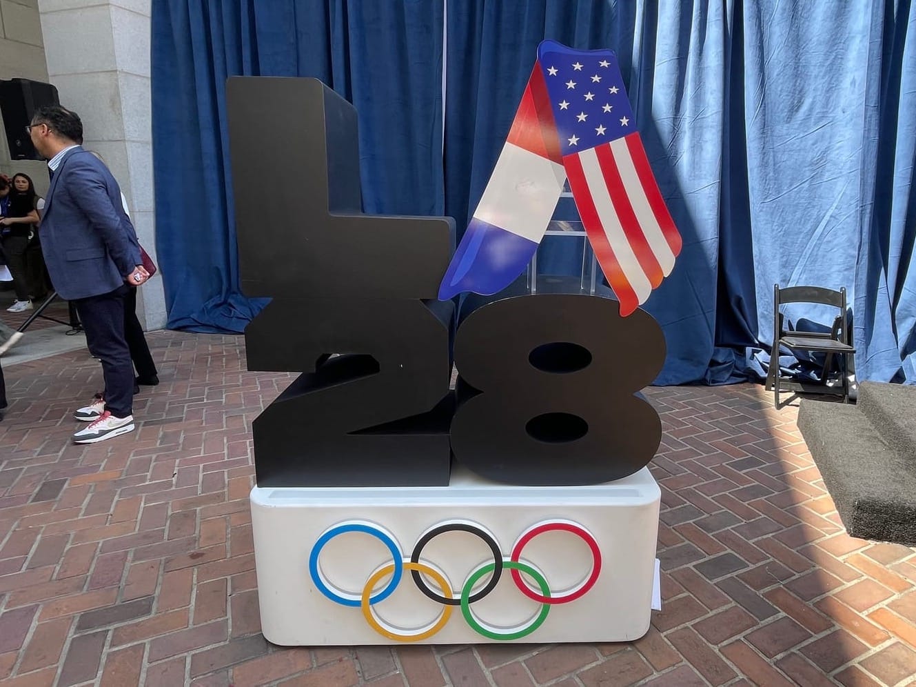 The LA28 logo with the French and U.S. flag and the Olympic rings below rendered as a 3D display at an event