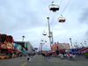 The Los Angeles County Fair's food booths, amusement rides, and a chairlift soaring overhead with gray skies