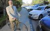 Donald Shoup, an older man with a beard and a suit, straddling his bike along a curb with paid parking spaces