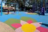 A beautiful new blue playground with kids on swings and a mat below with bright pink flowers 