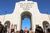 LA Mayor Karen Bass stands in a pink suit in the grand archway of the Coliseum with the Olympic rings above