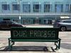 A green bus bench with graffiti reading "due process" on a busy LA street in the Koreatown neighborhood