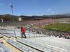 A fan walks through rows and rows of empty seats at the Rose Bowl stadium as soccer players take the field