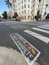 An intersection in LA's Koreatown shows newly painted crosswalks, one of which En Memoria de Nadir Gavarrete with fruits painted around it