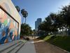 Three kids walking down a gravel path in a park with a large grassy hill, shade trees, and a colorful geometric mural