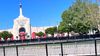 The LA Memorial Coliseum with the Olympic rings and the cauldron lit above surrounded by security fencing where a stadium worker is walking