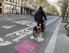 A person in a black coat rides a bike share bike in a pink Paris 2024-branded bike lane on a Paris street
