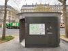 A public bathroom in Paris on the sidewalk with a large cabin and an open door, a map of the neighborhood, and water spigots
