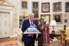 The fascist president Donald Trum, standing with Karen Bass, in the gilded Oval Office with a Palisades flag and Olympic torch