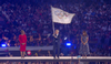 Mayor Karen Bass in a red suit, Thomas Bach holding the Olympic ring flag and Anne Hidalgo in a blue dress at the Paris closing ceremonies