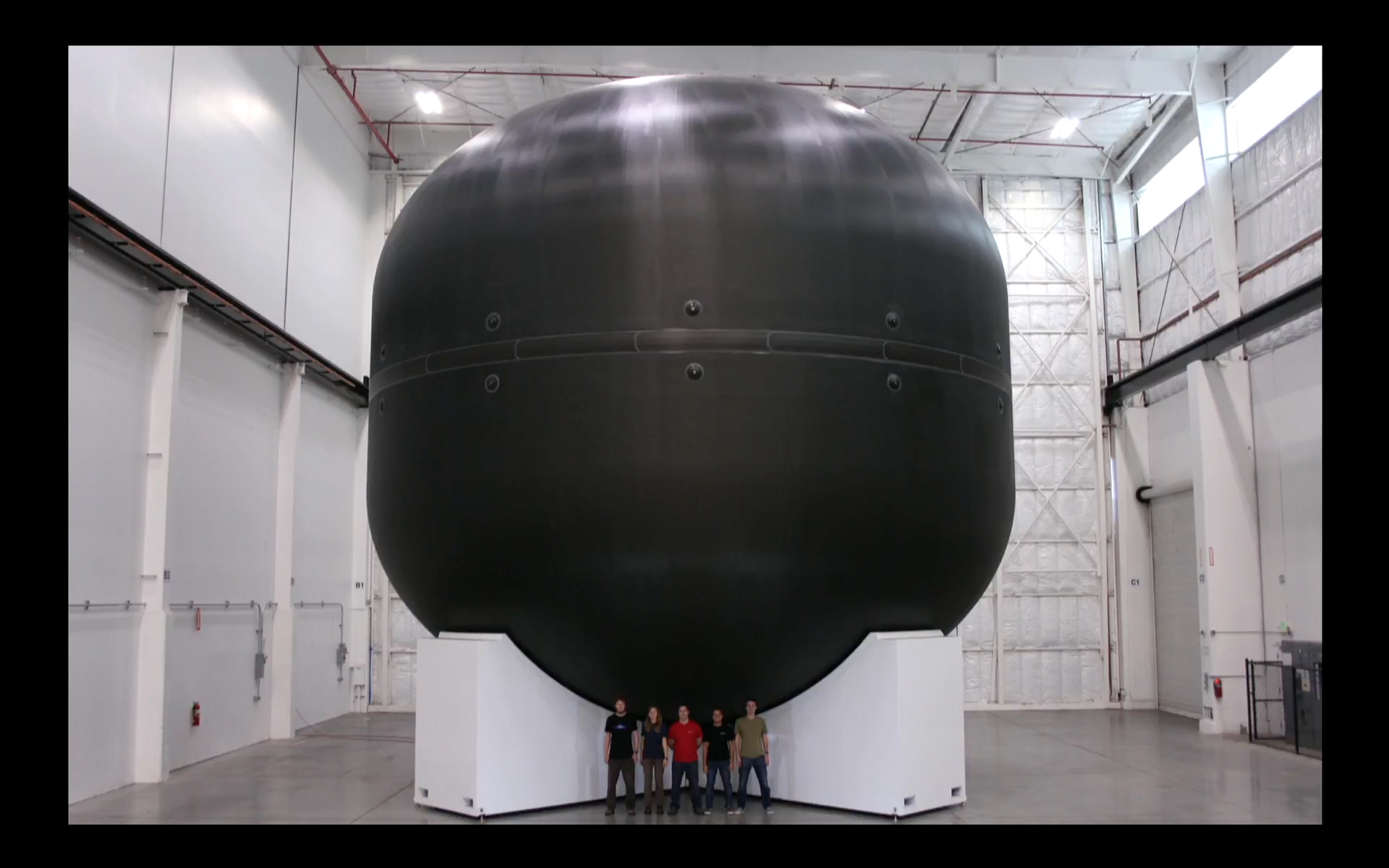 A group of people overshadowed by a huge carbon fiber tank.