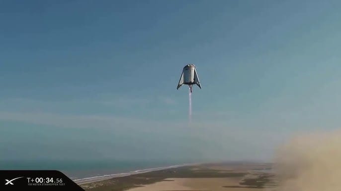 A stubby steel test rocket hovering over a beach in Texas.