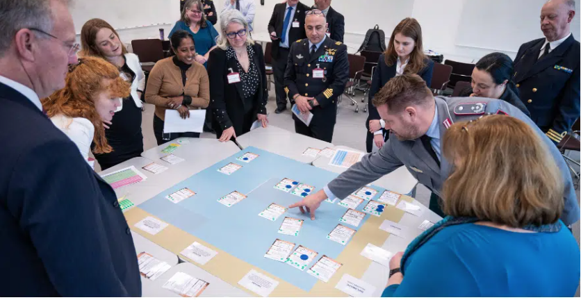 A bunch of people, some in uniform, meeting around a table with a war game on it.