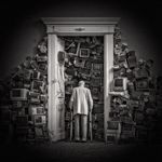 A figure with a walking frame stands at a doorway filled floor to ceiling with discarded monitors.