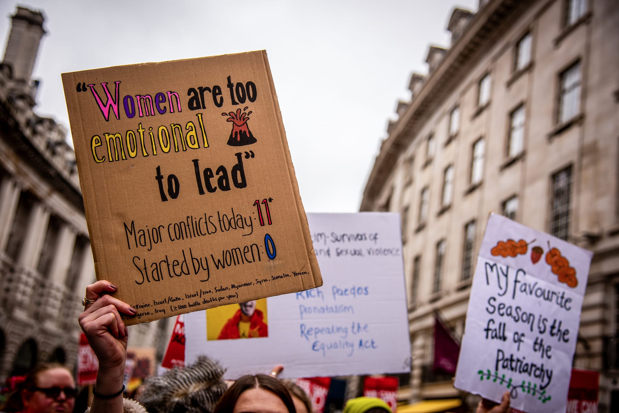 A rally placard reads "Women are too emotional to lead."