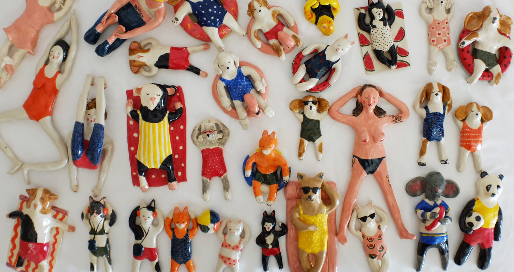 Ceramic figurines of cats, dogs and some ladies wearing swimsuits. They are sunbathing.