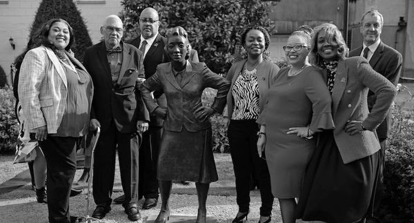 Photo of members of Henrietta Lacks' family, wearing business attire, surrounding a statue of Henrietta Lacks. 