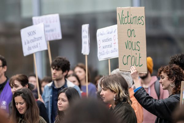A photograph of demonstrators holding up signs at a rally. One cardboard sign reads: Victimes on vous croit — Victims, we believe you