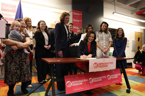 Gretchen Whitmer, surrounded by surrogacy advocates and their children, signs the new act into law