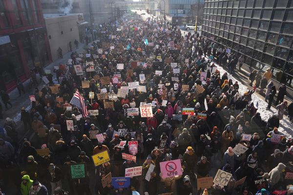 Photo of a large crowd in a built-up area. They carry signs including "ICE Out!", "GTFO", "Do You Hear The People Sing?" and "No Kings, No ICE". 