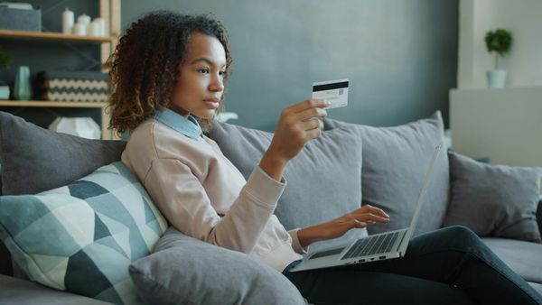 A woman with a laptop, sitting on the sofa, looking at her credit card.