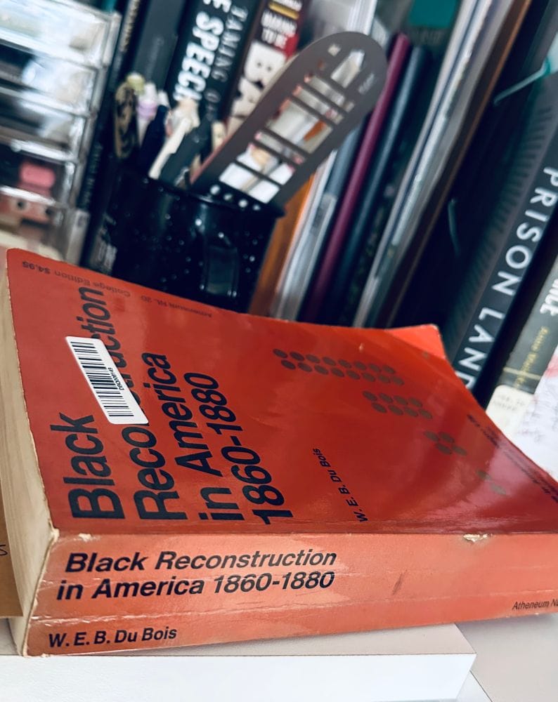 in front of a messy lineup of books and pens and papers, a copy of BLACK RECONSTRUCTION IN AMERICA, 1860-1880, by W. E. B. Du Bois