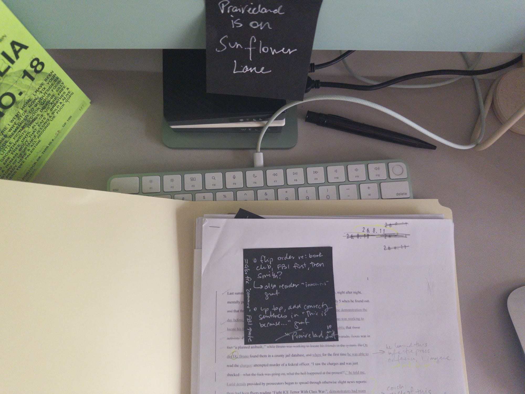 my desktop: an archival folder rests on a pearl grey desk mat. it is open to a printed draft with edit marks. a keyboard is beneath. a black post-it reads: PRAIRIELAND IS ON SUNFLOWER LANE