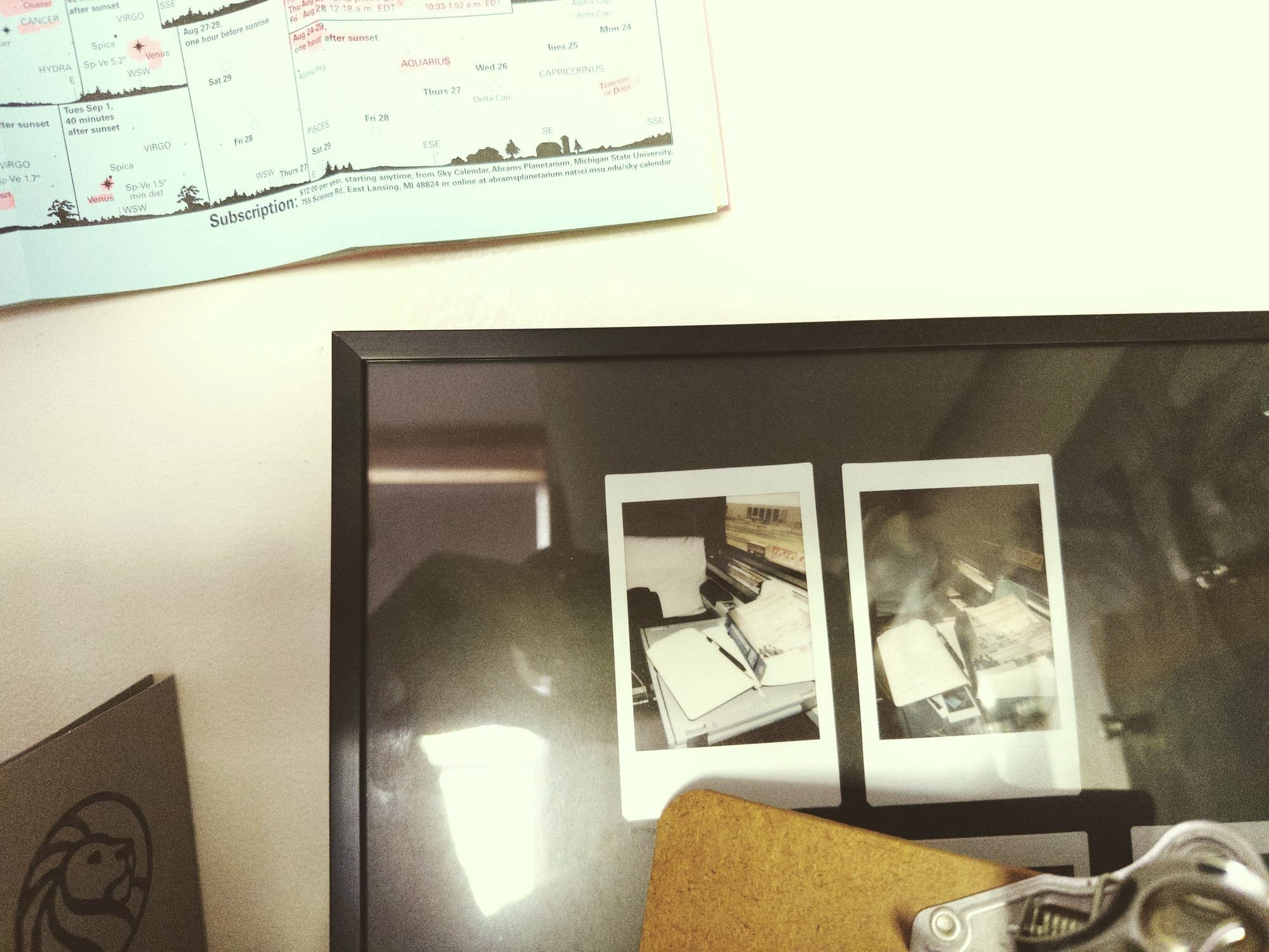 a frame askew leaning on a wall: two mini polaroids on a black mat, of books open on a train, the window outside. a star map above the frame, the folder with the lion logo for the NYPL to the left.