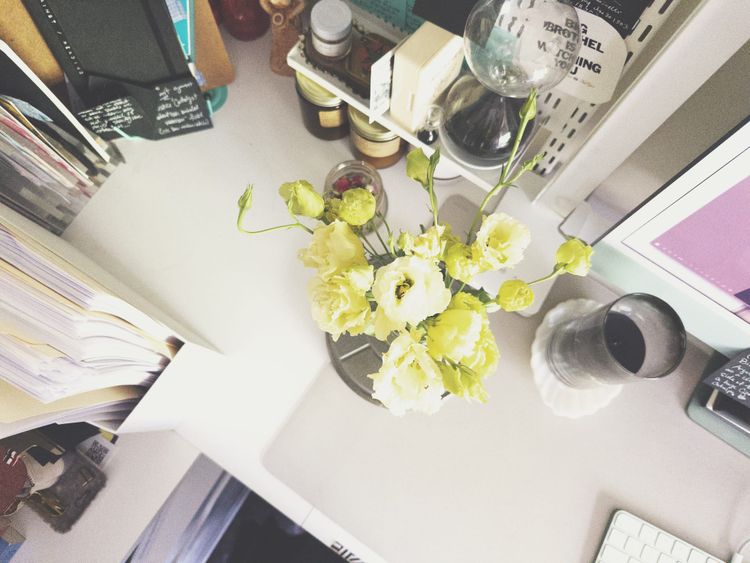 my desktop: a small arrangement of pale yellow flowers on a white desk, surrounded by archival file folders in a magazine holder, black post-it's, a black hourglass, a black candle, an iMac