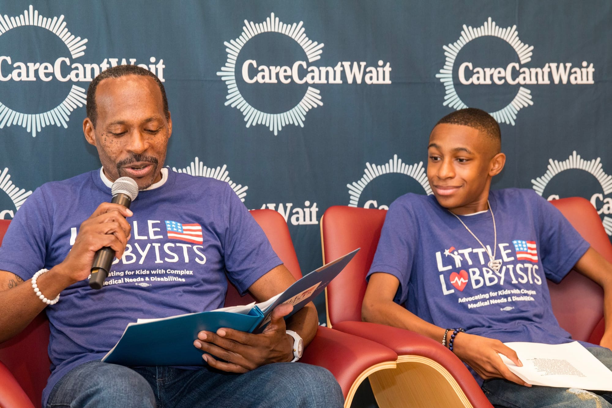 Rico &amp; Isra'El Winston speak at the summit. A Care Can't Wait backdrop is behind them, and they are seated, wearing primary blue Little Lobbyists t-shirts. Photo credit: Tirrea Billings 