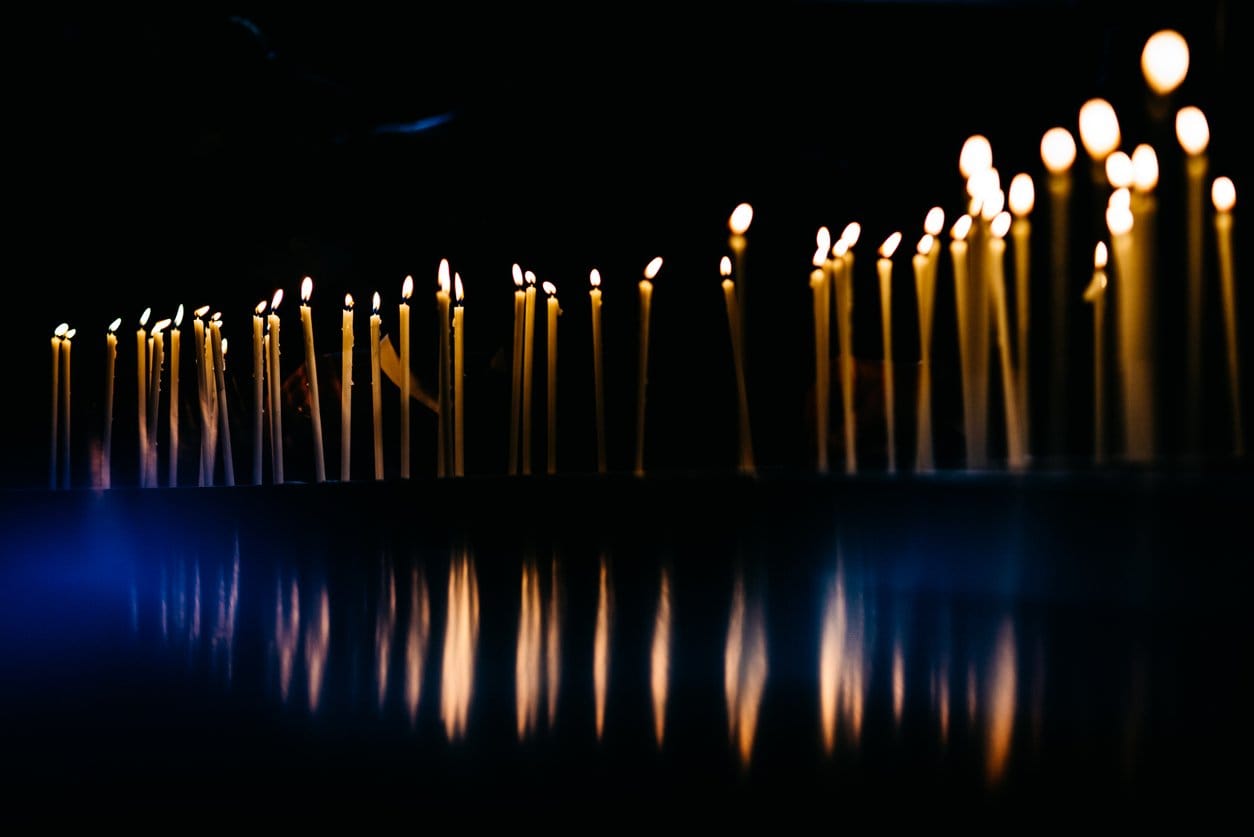 a line of candles lit in the darkness reflected in a dark surface below them.