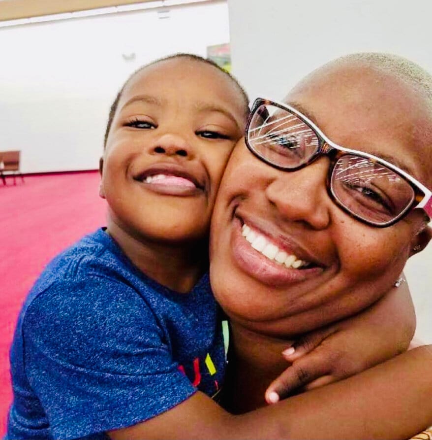 Anian &amp; Meeka [image description: A Black boy with Down Syndrome hugs his mom, who wears glasses and has short light hair.
